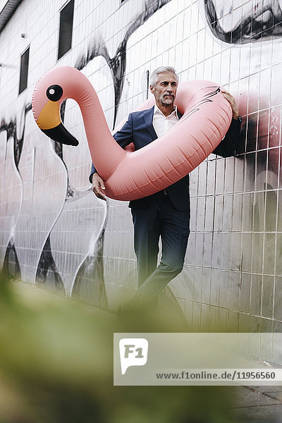 Mature businessman outdoors with inflatable flamingo