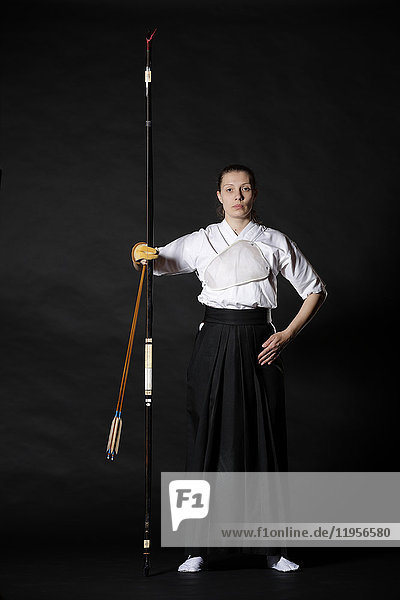 Caucasian woman practicing traditional Kyudo Japanese archery on black background