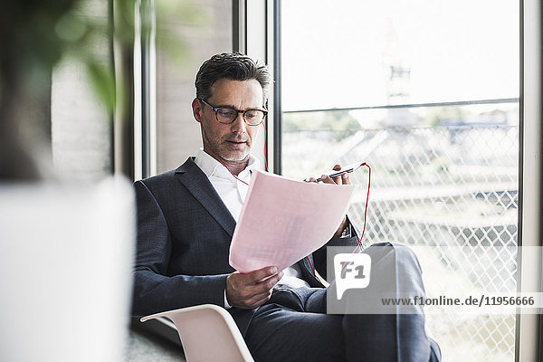 Businessman reading documents and speaking notes on smartphone