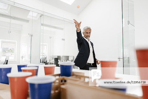 Mature businessman with architectural model in office throwing a ball