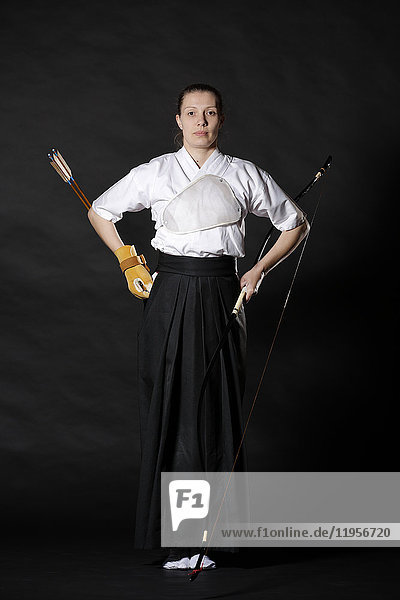 Caucasian woman practicing traditional Kyudo Japanese archery on black background