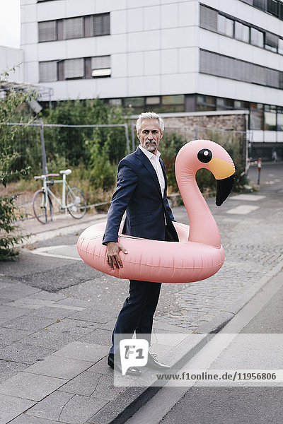 Mature businessman on the street with inflatable flamingo