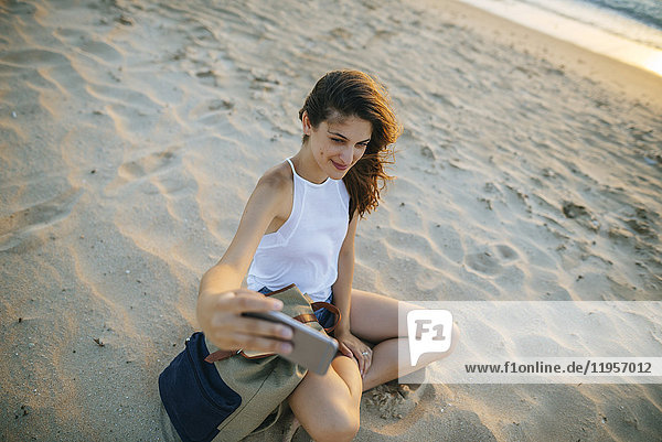 Junge Frau  die einen Selfie mit einem Smartphone am Strand nimmt