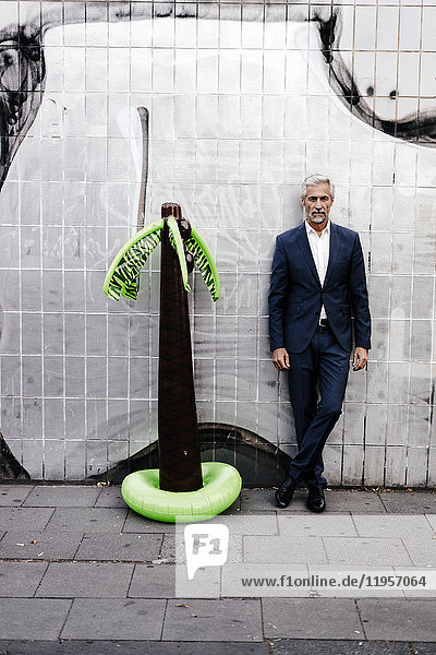 Mature businessman outdoors with inflatable palm tree