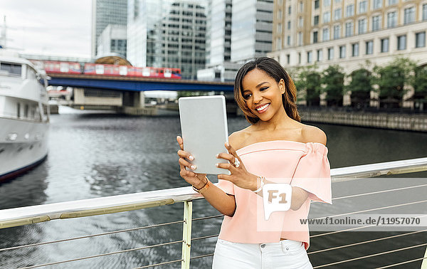 Lächelnde Frau  die einen Selfie mit ihrer Tafel in der Stadt nimmt.