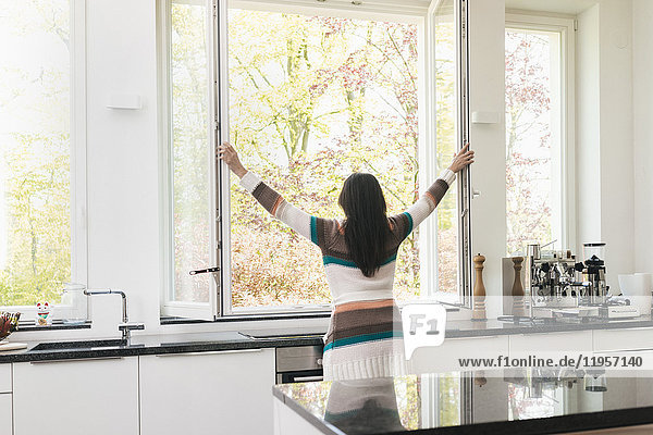Frau in der Küche öffnet das Fenster
