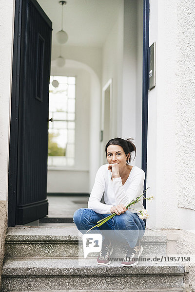 Frau mit Blumen auf der Türschwelle sitzend