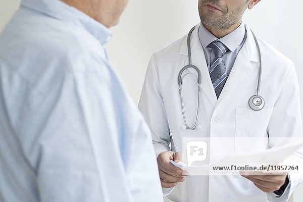 MODELL FREIGEGEBEN. Männlicher Arzt mit medizinischen Notizen im Gespräch mit einem älteren Patienten.