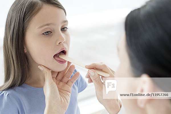 Female doctor examining inside girl's mouth.