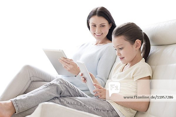 Mutter und Tochter auf dem Sofa mit digitalen Tablets.