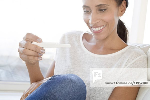 Mittlere erwachsene Frau mit Schwangerschaftstest in der Hand  lächelnd.