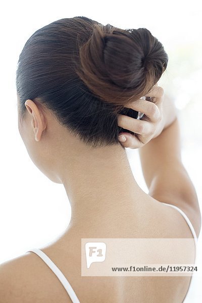 Young woman with hair bun scratching head.