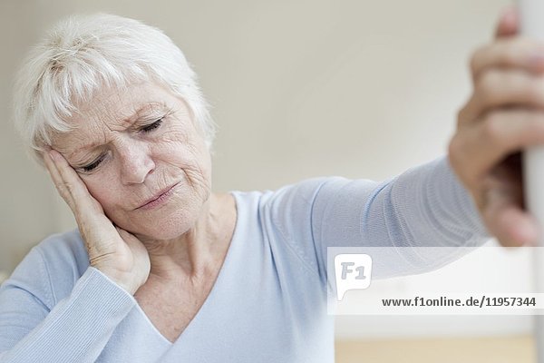 MODELL FREIGEGEBEN. Ältere Frau mit Kopfschmerzen  an die Wand gelehnt.