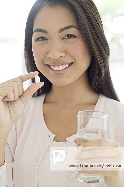Junge Frau mit Pille und Glas Wasser in der Hand.