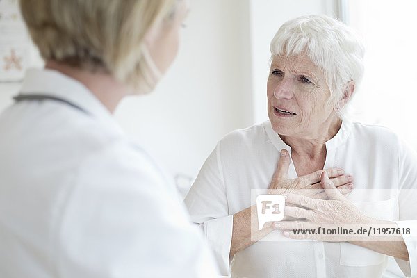 MODELL FREIGEGEBEN. Ältere Frau berührt die Brust und spricht mit einer Ärztin.