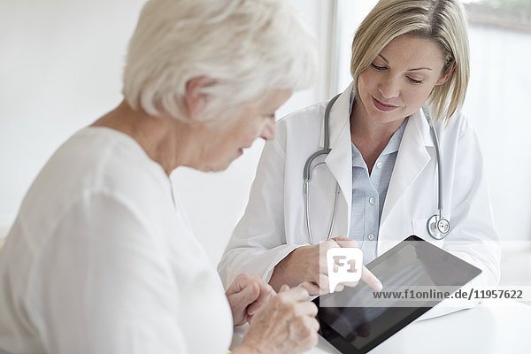 MODELL FREIGEGEBEN. Ärztin zeigt älteren Patienten Röntgenbild der Hand auf digitalem Tablet.