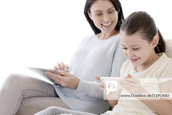 Mutter und Tochter auf dem Sofa mit digitalem Tablet und Smartphone.