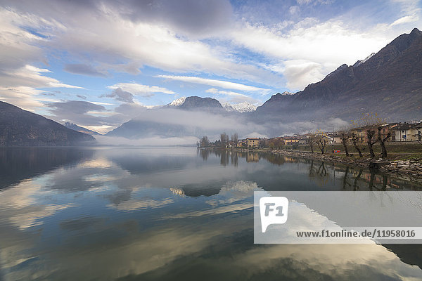Mountains and village are reflected in Lake Mezzola at dawn shrouded by mist  Verceia  Chiavenna Valley  Lombardy  Italy  Europe