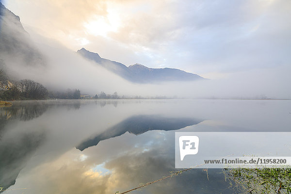 Mountains reflected in water at dawn shrouded by mist  Pozzo di Riva Novate  Mezzola  Chiavenna Valley  Lombardy  Italy  Europe