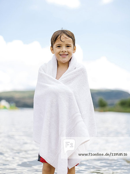 Portrait of boy (6-7) wrapped in towel standing by lake