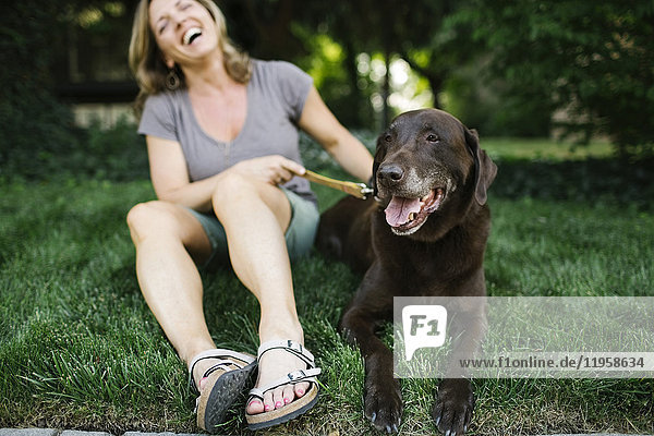 Lächelnde Frau im Gras sitzend mit Labrador Retriever