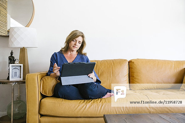 Frau benutzt digitales Tablet auf Sofa