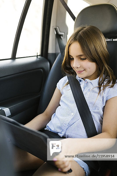 Mädchen ( 8-9) sitzt im Auto und benutzt ein digitales Tablet