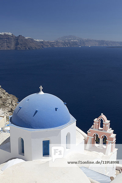 Weiße Kirche mit blauer Kuppel und rosa Glockenturm mit Blick auf die Caldera  Oia  Santorin  Kykladen  Griechische Inseln  Griechenland  Europa
