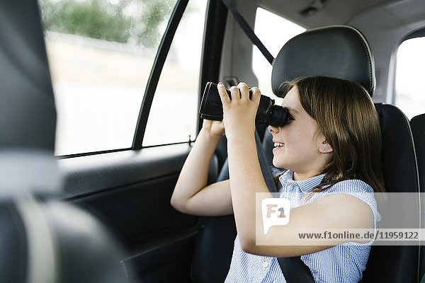 Mädchen ( 8-9) sitzt im Auto und schaut durch ein Fernglas