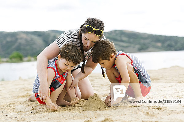 Mother playing with sons (4-5  6-7) on beach by lake