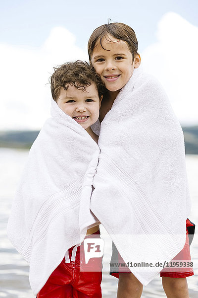 Portrait of brothers (4-5  6-7) wrapped in towels standing by lake