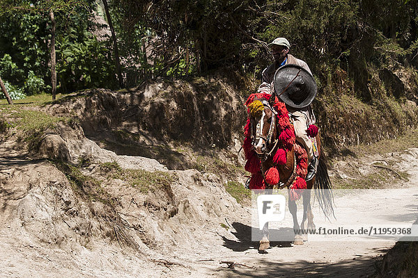 Ein Mann reitet auf einem Pferd mit traditionellem roten und gelben äthiopischen Kopfschmuck und trägt ein traditionelles Rundschild  Äthiopien  Afrika