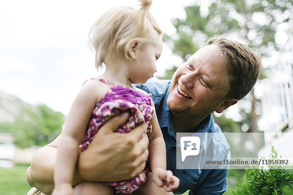 Vater spielt mit einem kleinen Mädchen (12-17 Monate) im Hinterhof