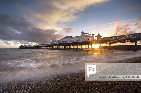 Brighton Pier bei Sonnenuntergang mit dramatischem Himmel und Wellen  die an den Strand gespült werden  Brighton  East Sussex  England  Vereinigtes Königreich  Europa