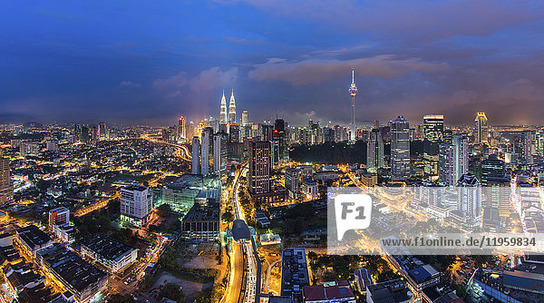 Stadtlandschaft von Kuala Lumpur  Malaysia in der Abenddämmerung  mit beleuchteten Petronas-Türmen und Kommunikationsturm in der Ferne.