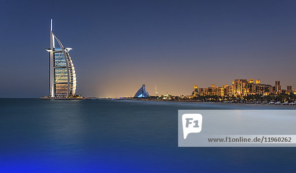 Stadtbild von Dubai  Vereinigte Arabische Emirate in der Abenddämmerung  Küstenlinie des Persischen Golfs mit dem beleuchteten Wolkenkratzer Burj Al Arab in der Ferne.