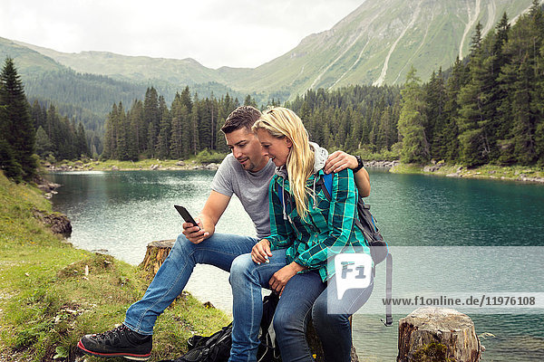 Couple hiking  sitting by lake looking at smartphone  Tirol  Steiermark  Austria  Europe