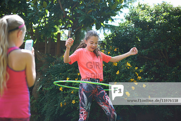 Girl photographing teenage sister hoola hooping in garden