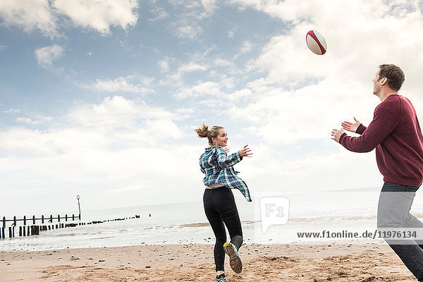Vater und Tochter spielen Rugby am Strand