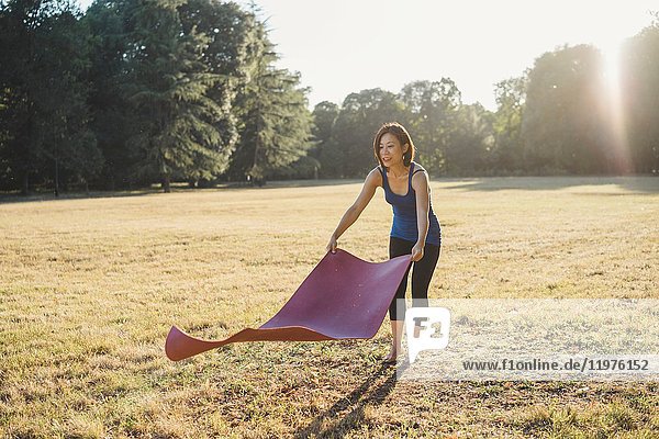 Mature woman in park  laying yoga mat on grass