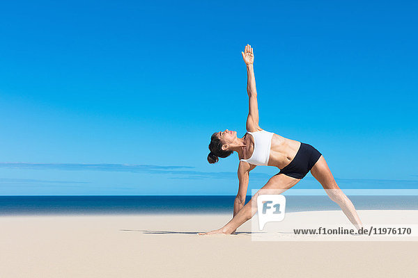 Frau am Strand beugt die Arme seitlich ab und hebt sie in Yogastellung an