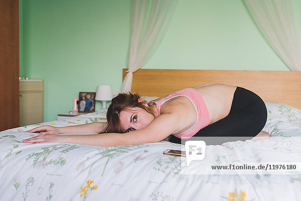 Junge Frau praktiziert Yoga  indem sie sich auf dem Bett nach vorne beugt