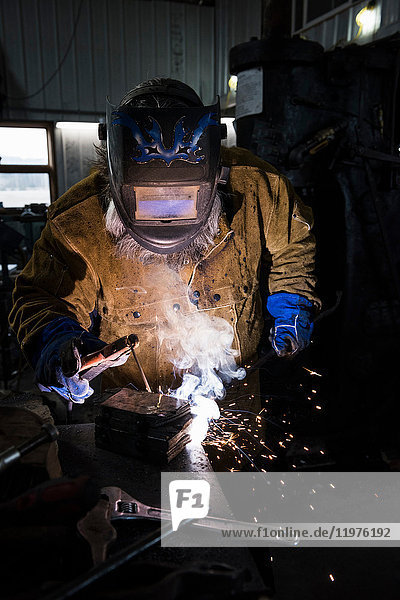 Schmied in Schweißmaske schweißt Metall in Werkstatt