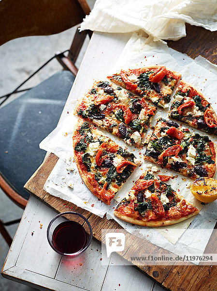 Geschnittene Spinat- Feta- und Olivenpizza auf Servierbrett erhöhte Ansicht