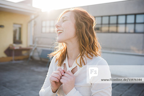 Junge Frau mit roten Haaren lacht auf sonnenbeschienener Dachterrasse