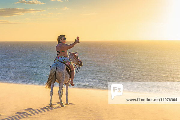 Frau reitet auf einem Pferd am Strand  fotografiert die Aussicht mit einem Smartphone  Jericoacoara  Ceara  Brasilien  Südamerika