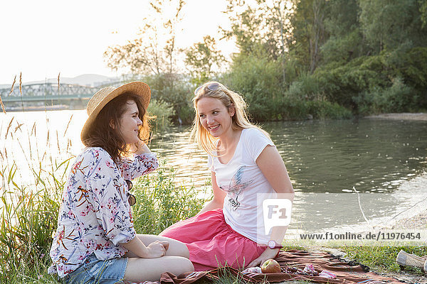 Two female friends relaxing beside lake