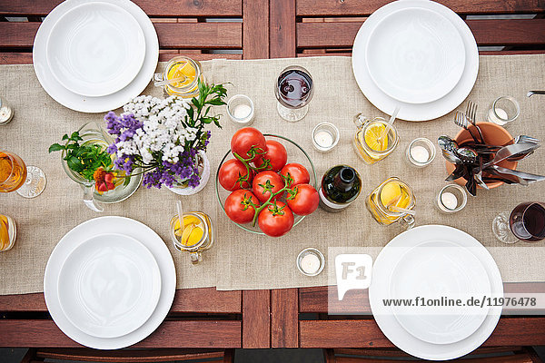 Draufsicht auf einen Tisch mit Blumen und Strauchtomaten zum Mittagessen auf der Terrasse