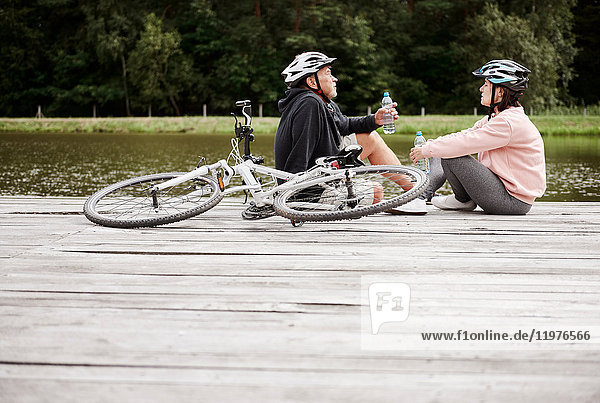 Mature couple relaxing on jetty beside lake  bicycles behind them
