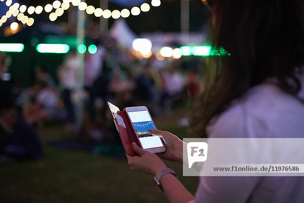 Reife Frau begutachtet Smartphone-Fotos auf dem Nachtmarkt-Festival im Park  London  Großbritannien